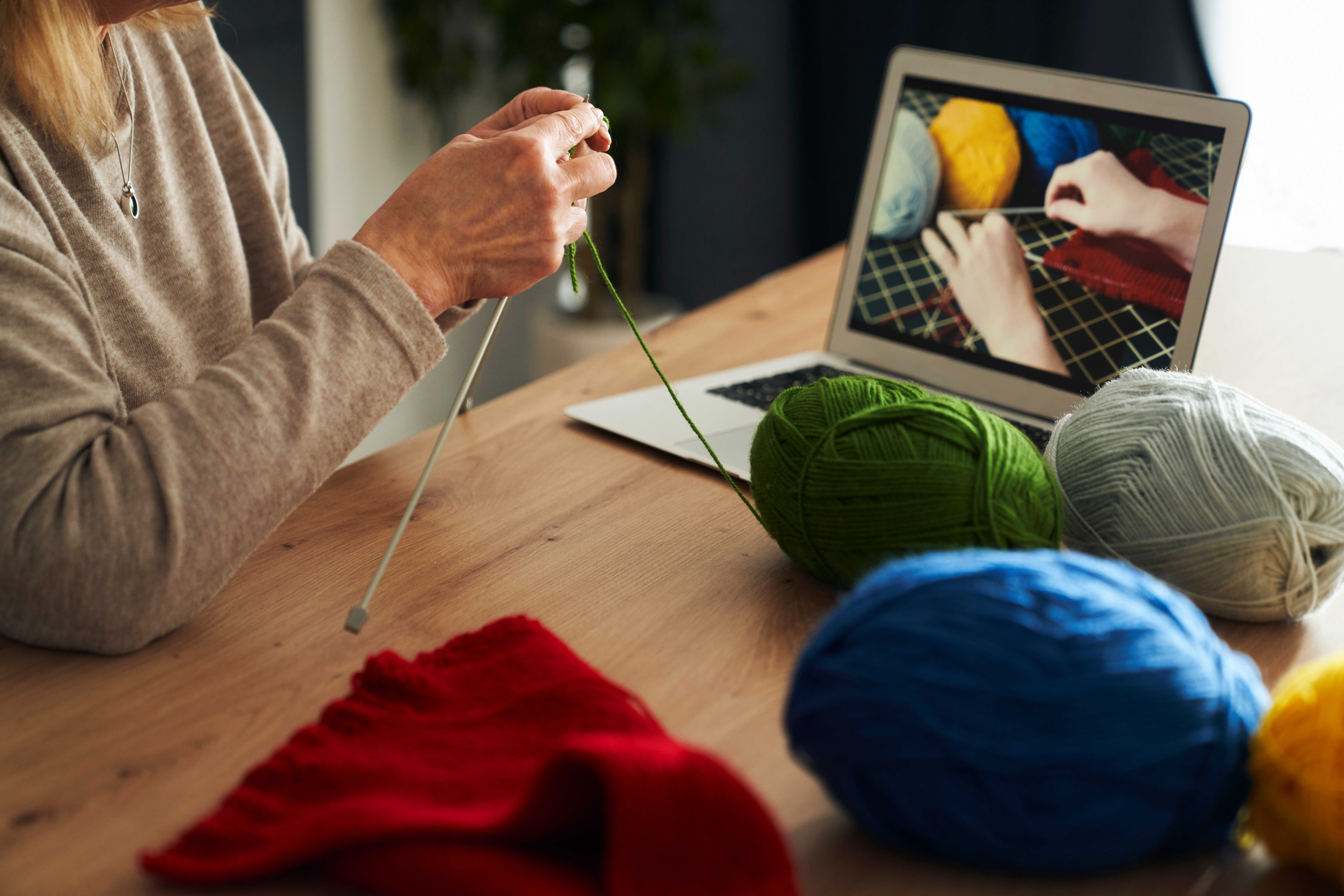 Close up of caucasian senior woman at home learning how to knit from video tutorial